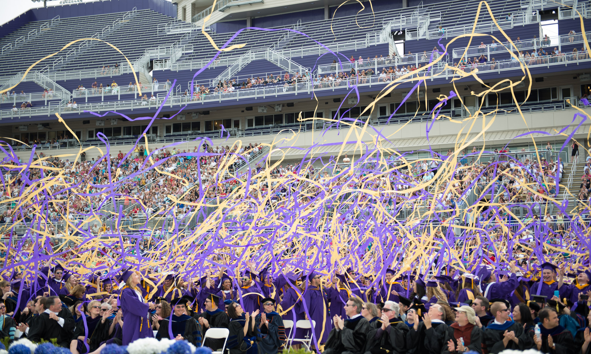 Class of 2014 graduates throw purple and gold streamers in celebration.